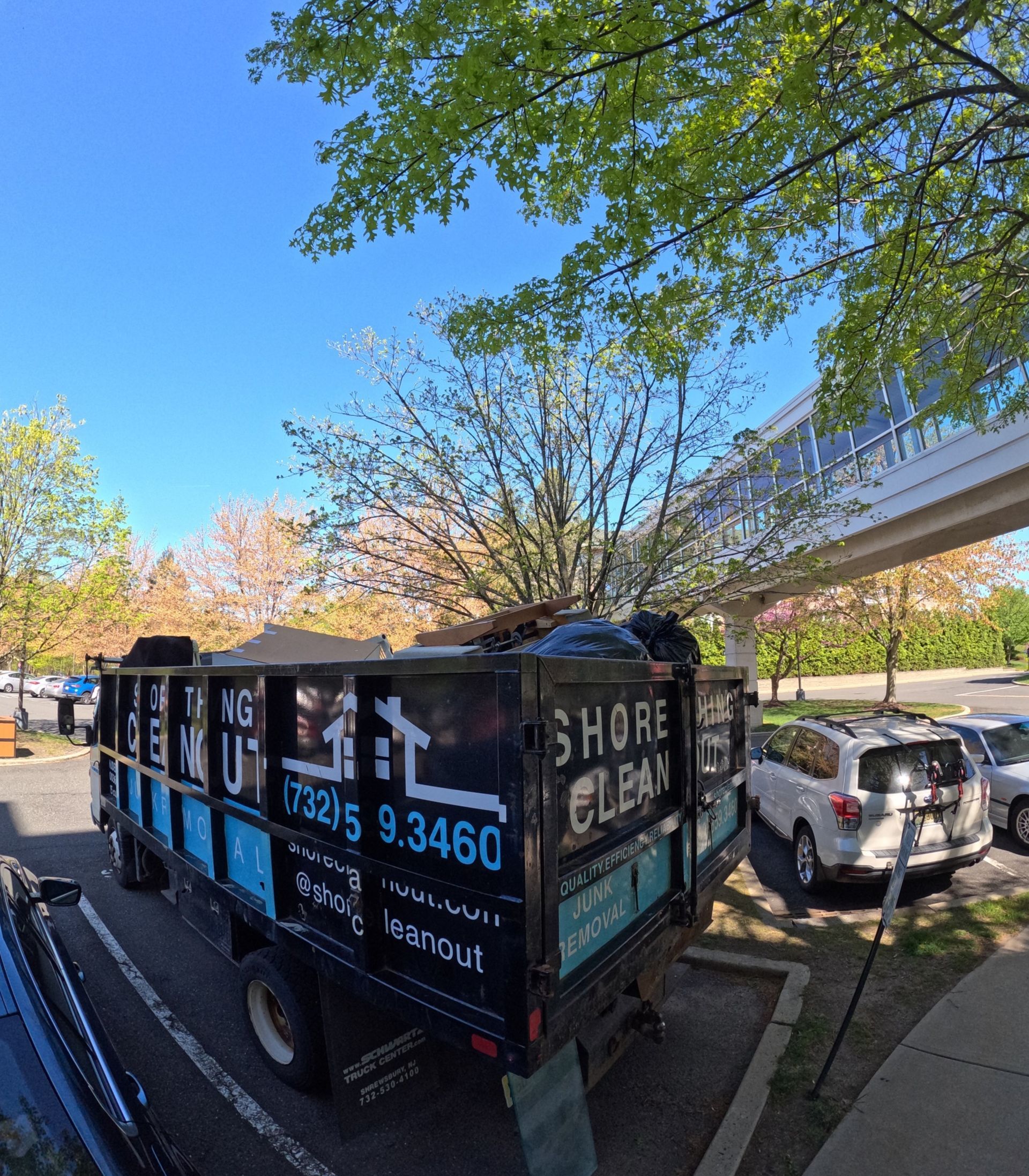 Dump truck with "Shore Clean" logo parked under a tree-lined sky.