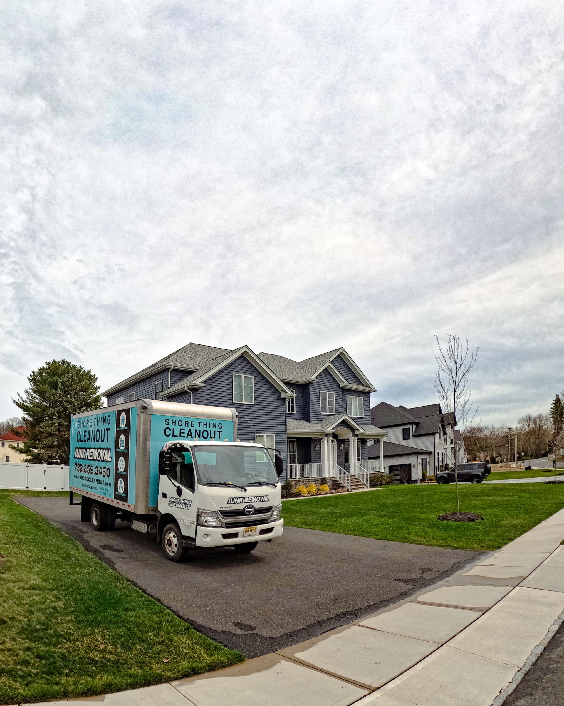 A moving truck parked in a driveway in front of a blue house with cloudy sky.