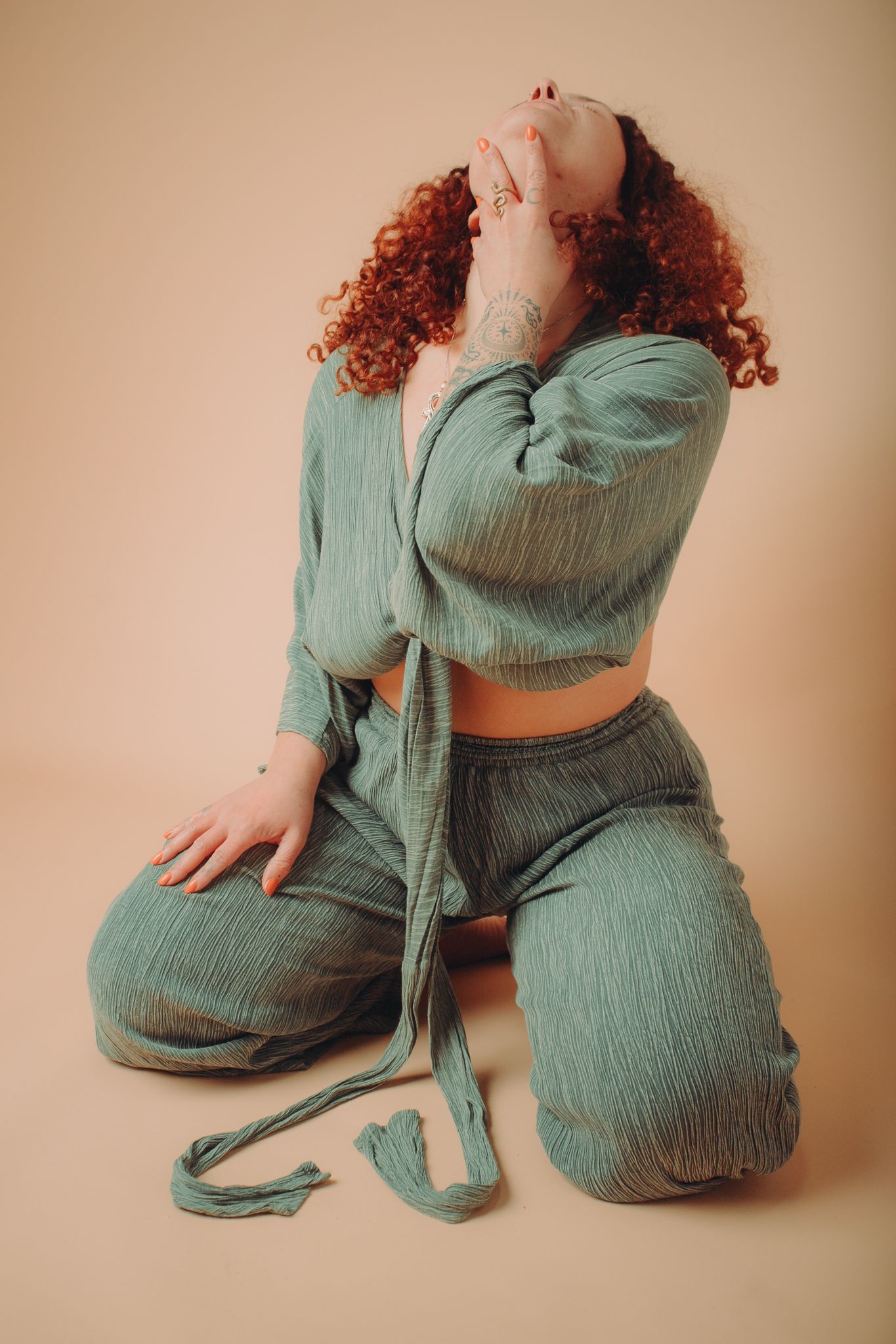 A woman with red curly hair is kneeling down and covering her face with her hand.
