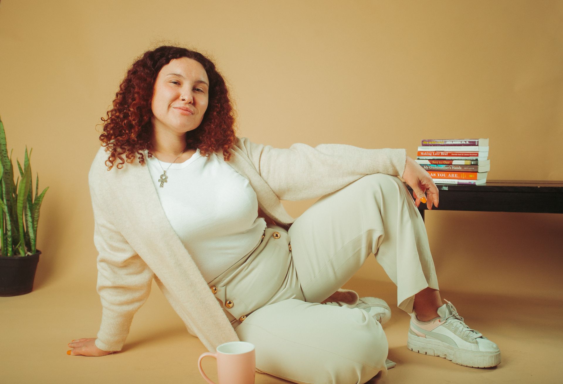 A woman is sitting on the floor next to a stack of books.