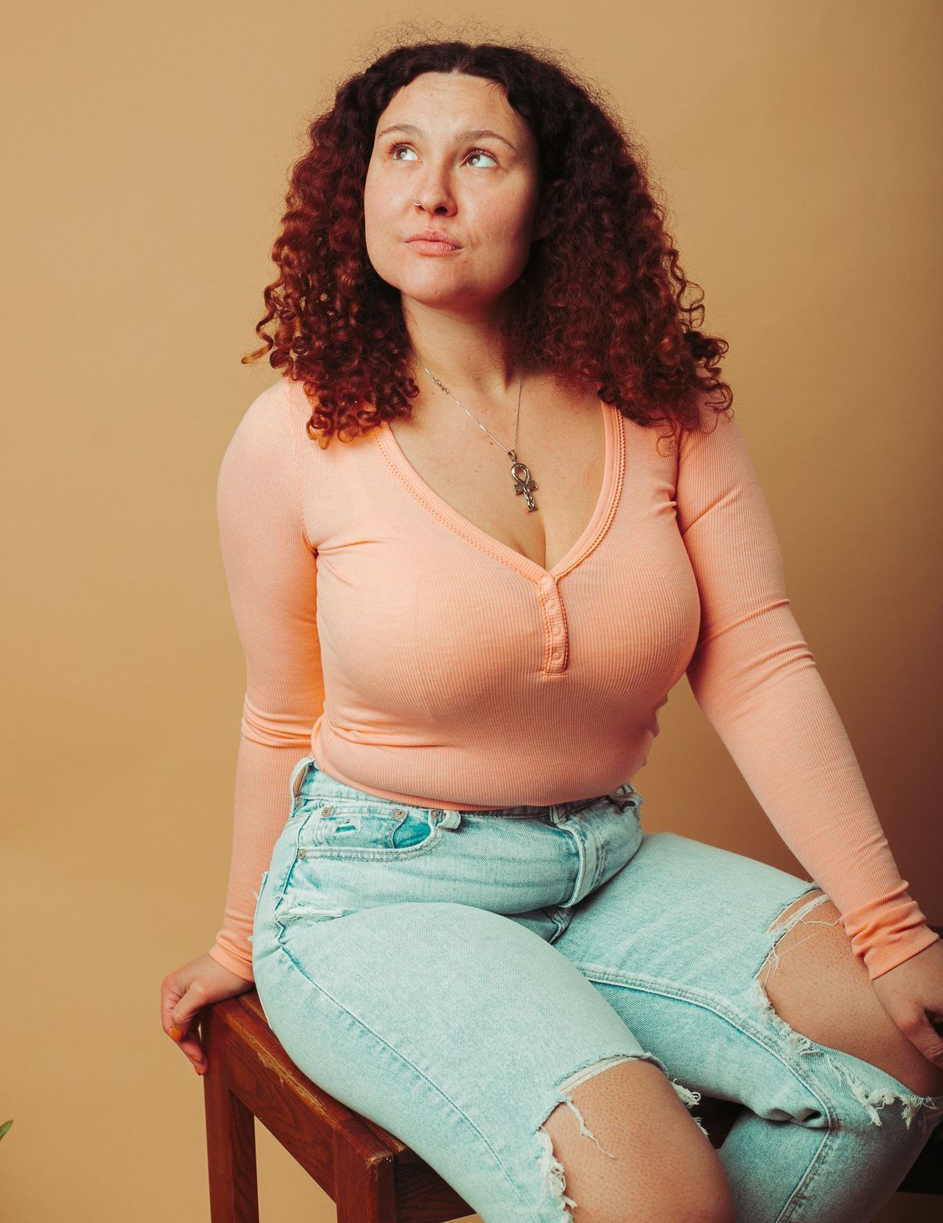 A woman with curly hair is sitting on a wooden stool.