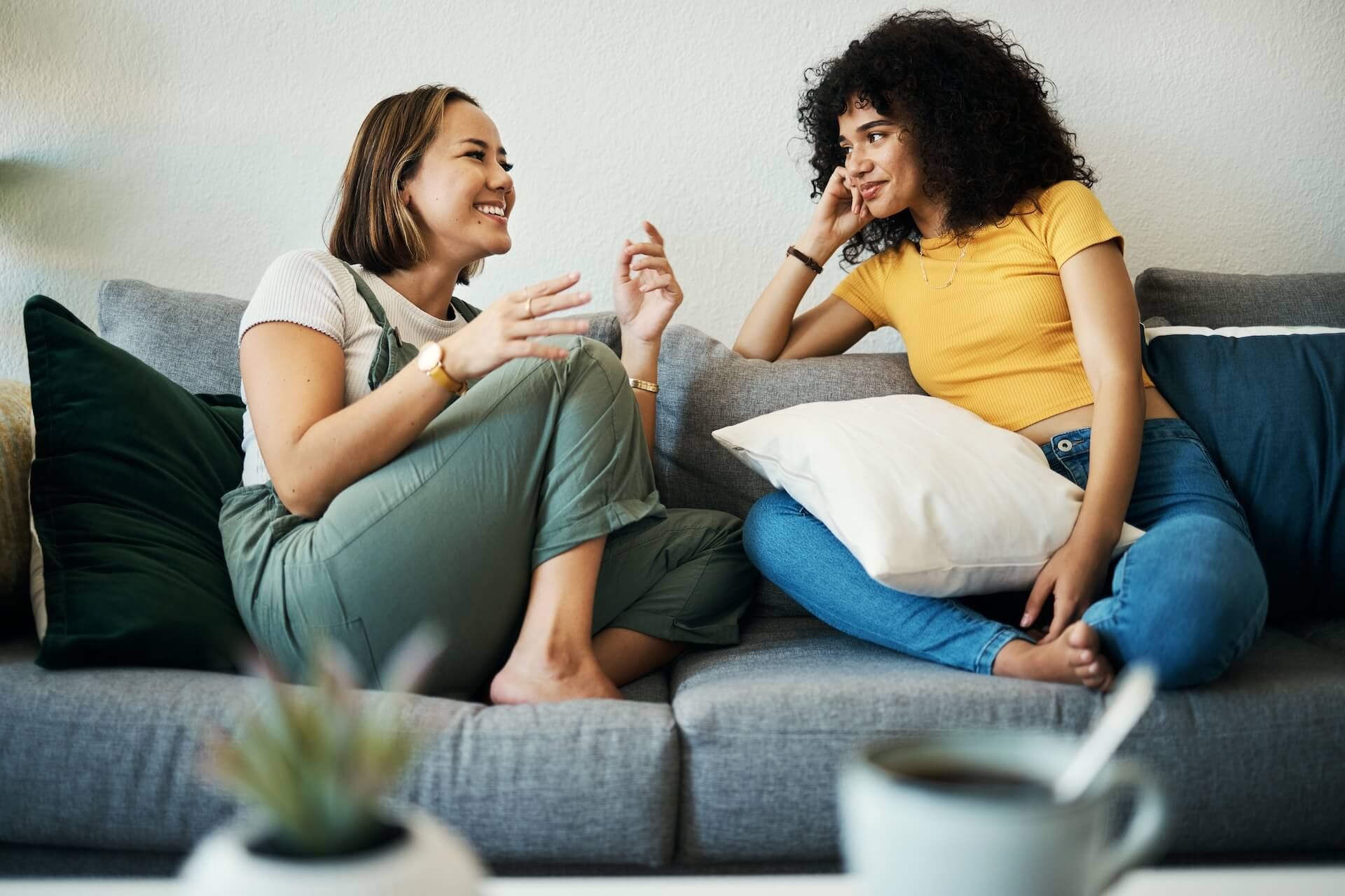 Two women are sitting on a couch talking to each other.
