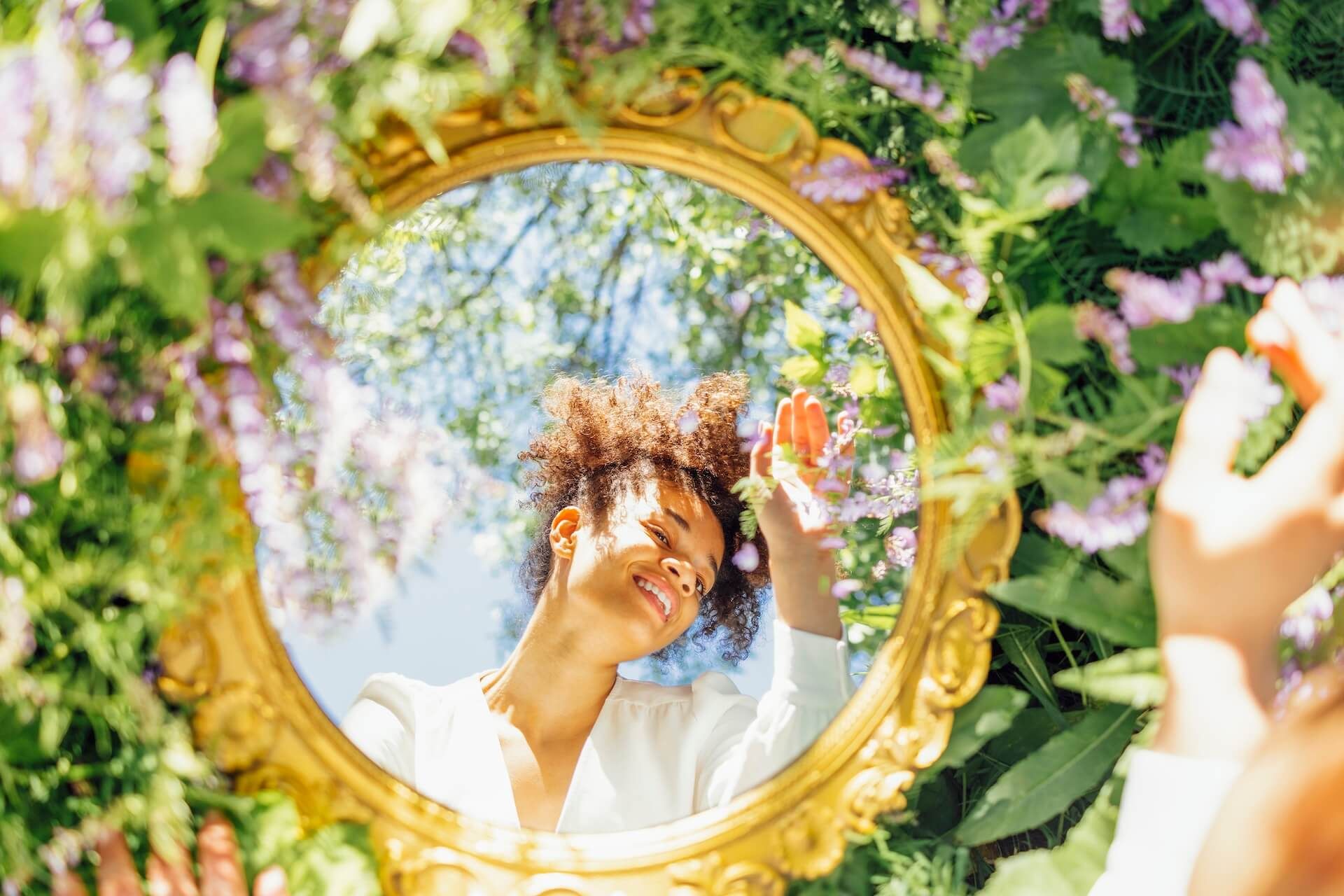 A woman is looking at her reflection in a mirror surrounded by flowers.