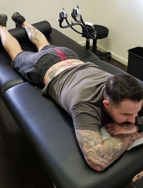 Man lying face down on a tattoo table, receiving a tattoo on his back.