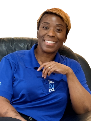Dr. Natasha Williams in blue polo smiling, sitting in a black chair, with short blonde hair.