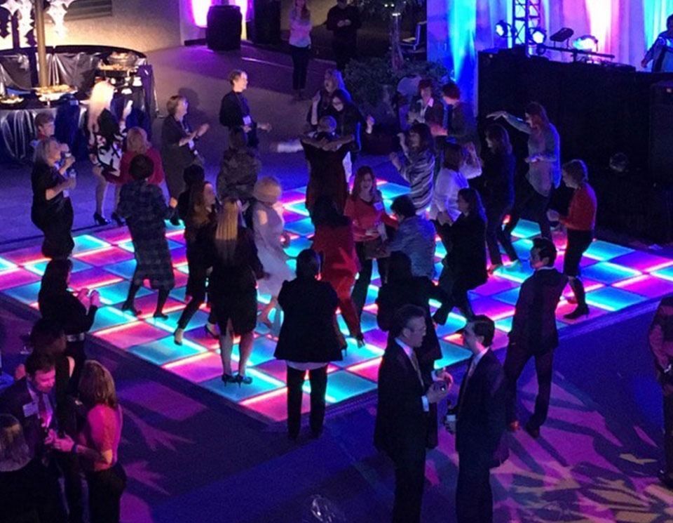People dancing on a colorful, illuminated dance floor at an outdoor event.