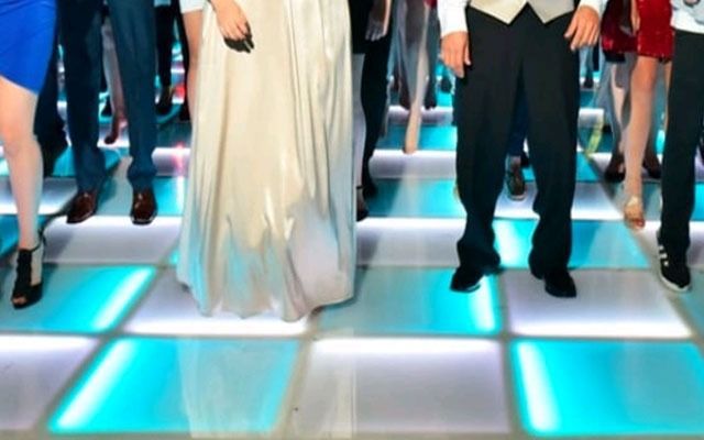 People dancing on a lit, blue and white tiled dance floor.