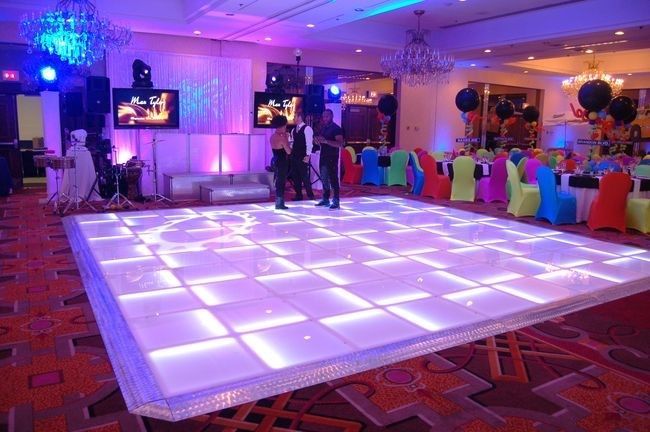 Lit-up dance floor in a ballroom with a band, colorful chairs, and decor. Stage with screens and purple lighting.