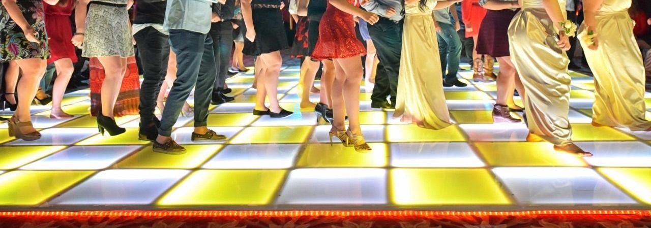 People dancing on a checkered illuminated dance floor at a club.