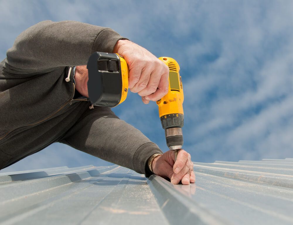 Man Using an Electric Drill to Fasten Down a Metal Roof — Roof Painting in Wingham, NSW