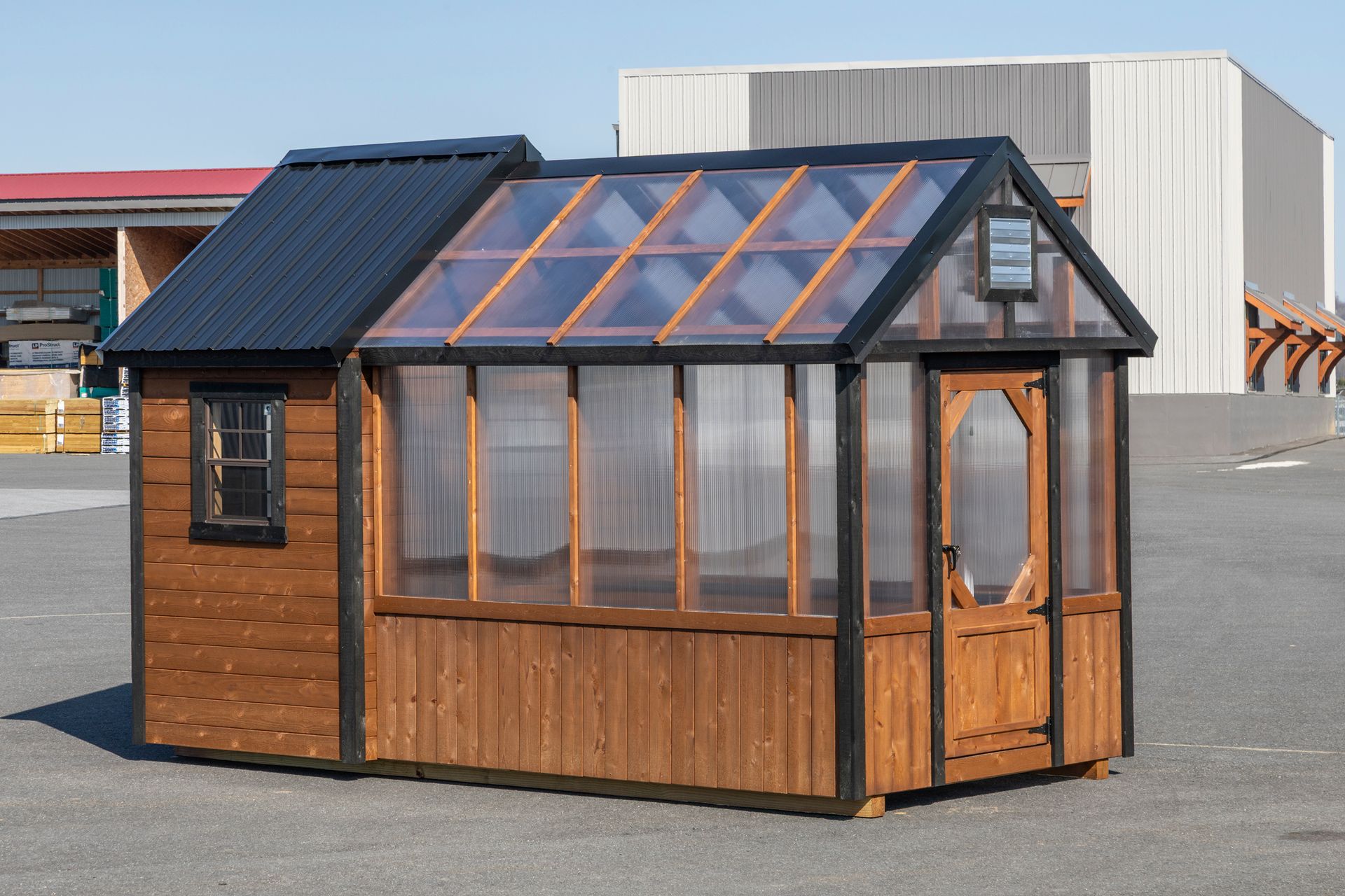 A small, wooden greenhouse hybrid structure with a solid metal-roofed section and a glass-paneled greenhouse area.