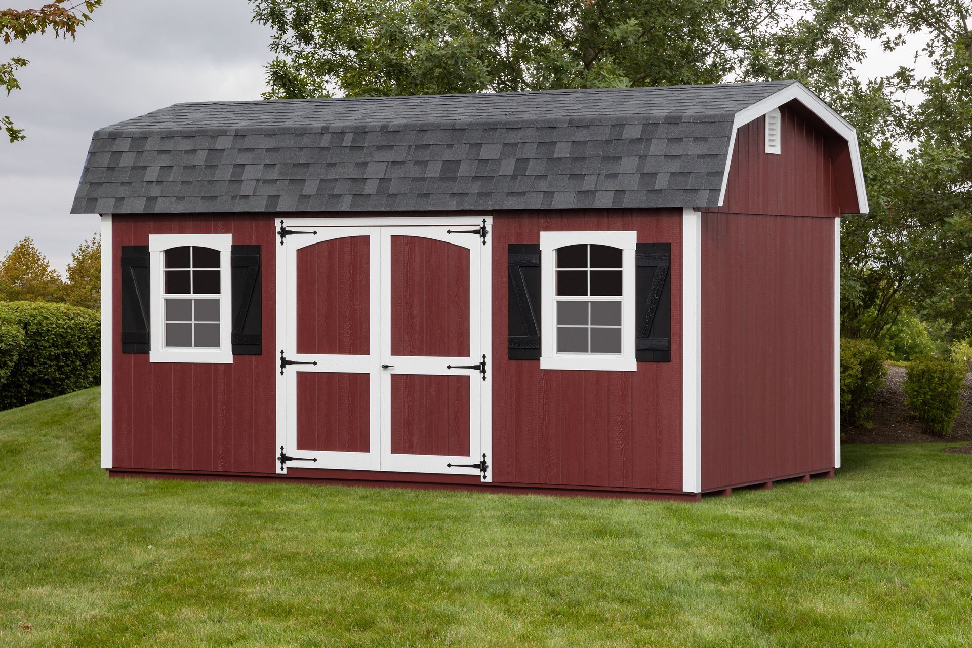 Red shed with white trim, black shutters, and double doors on green grass.