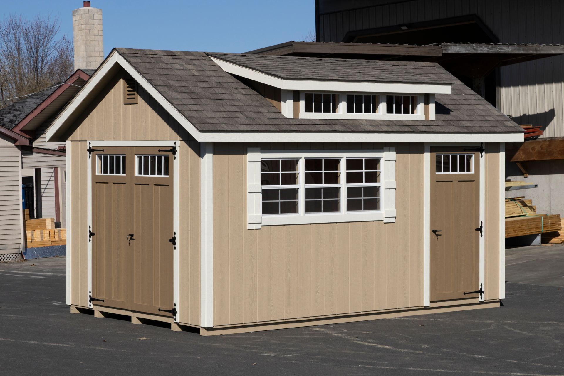 Tan storage shed with brown doors, white window trim, and a dormer.