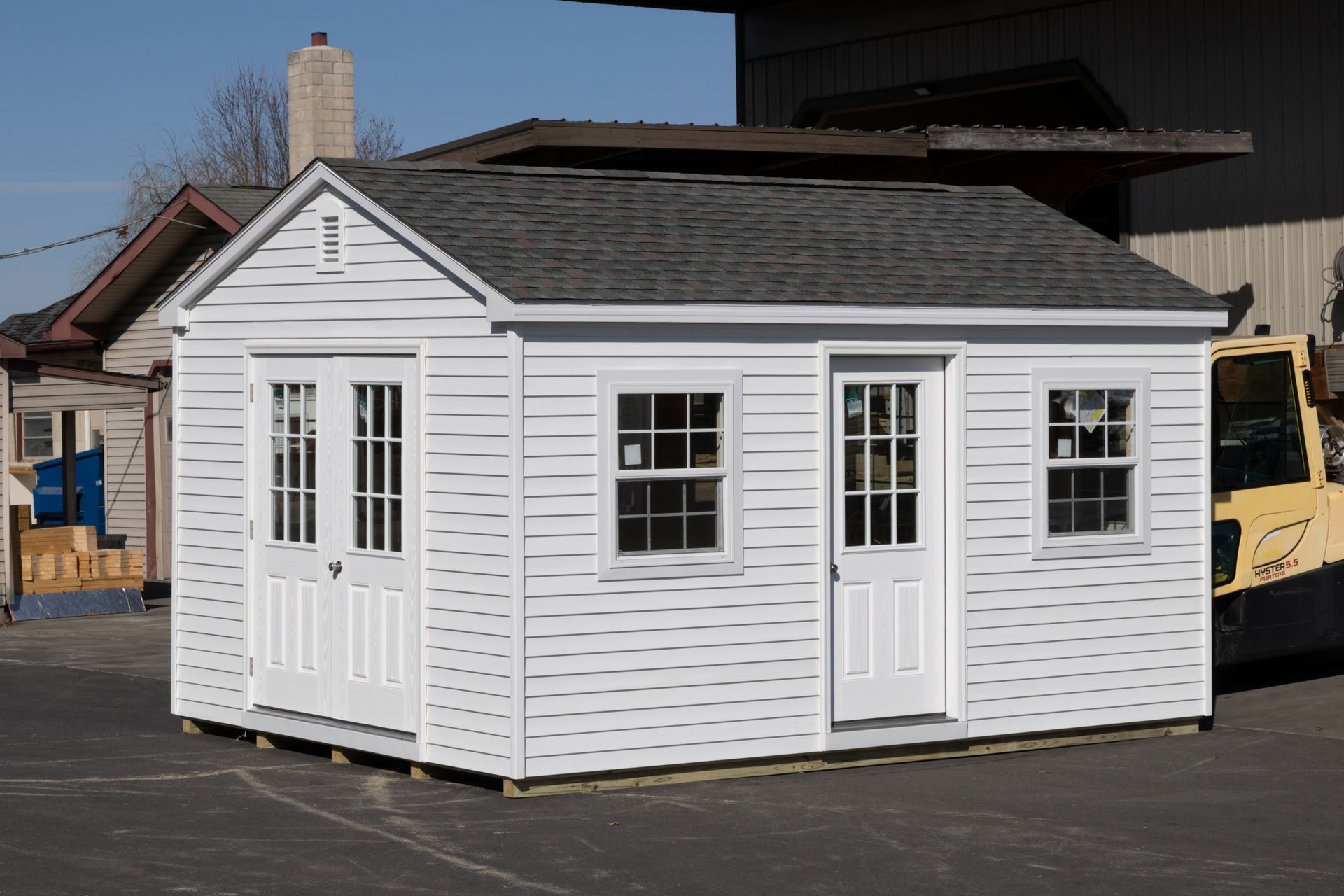 White shed with dark gray roof, two doors, and two windows.