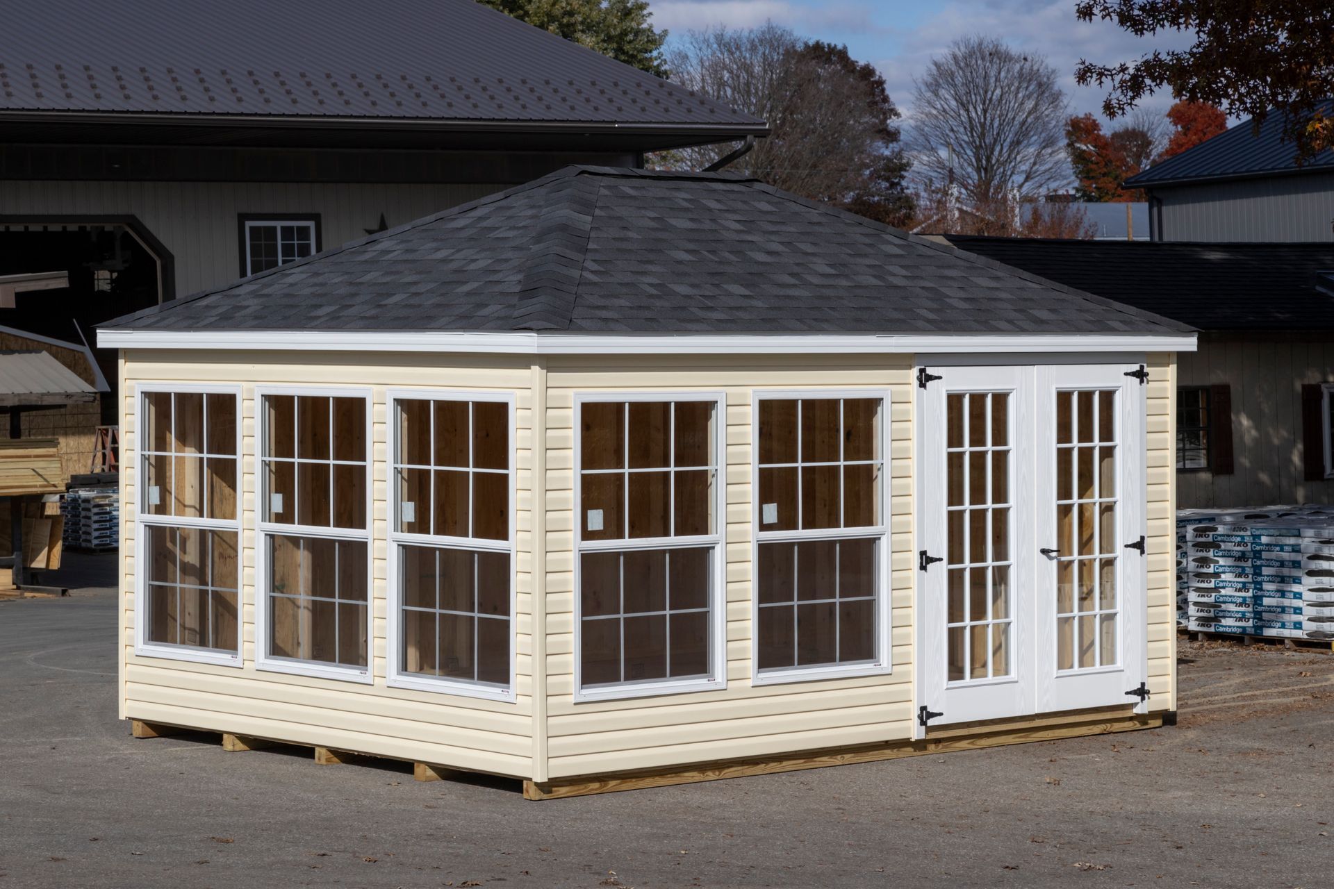 Tan-sided gazebo with black roof, windows, and white French doors. Outdoors on a concrete surface.
