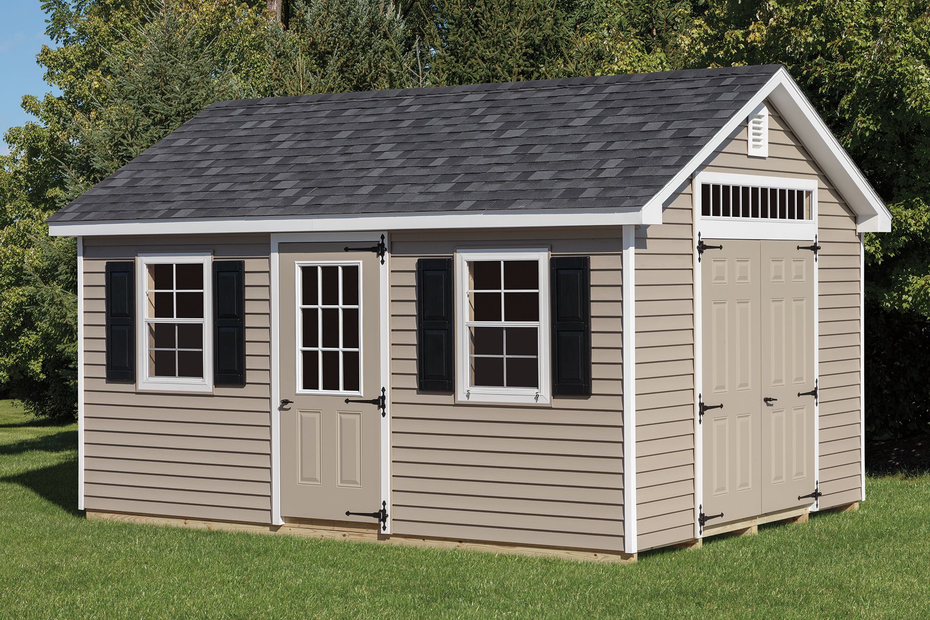 Tan storage shed with black shutters, gray roof, and beige doors, set on a green lawn.
