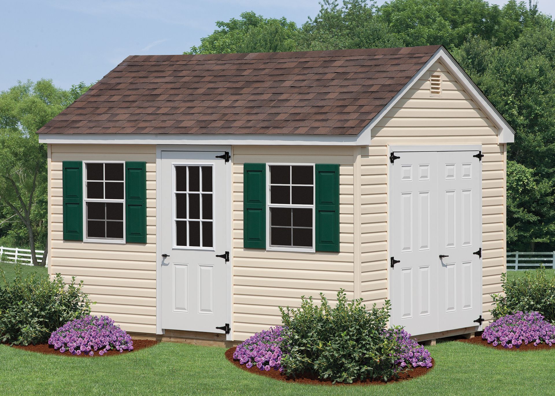 Tan shed with brown roof, green shutters, white doors, and purple flowers.