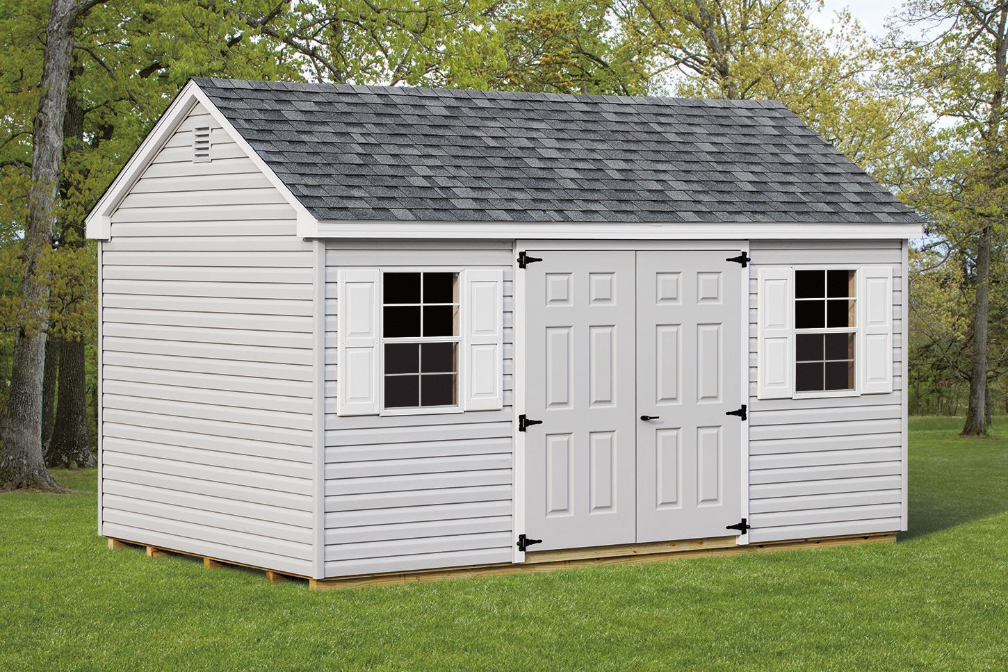 White shed with gray roof, two windows, double doors, and white shutters on grass.