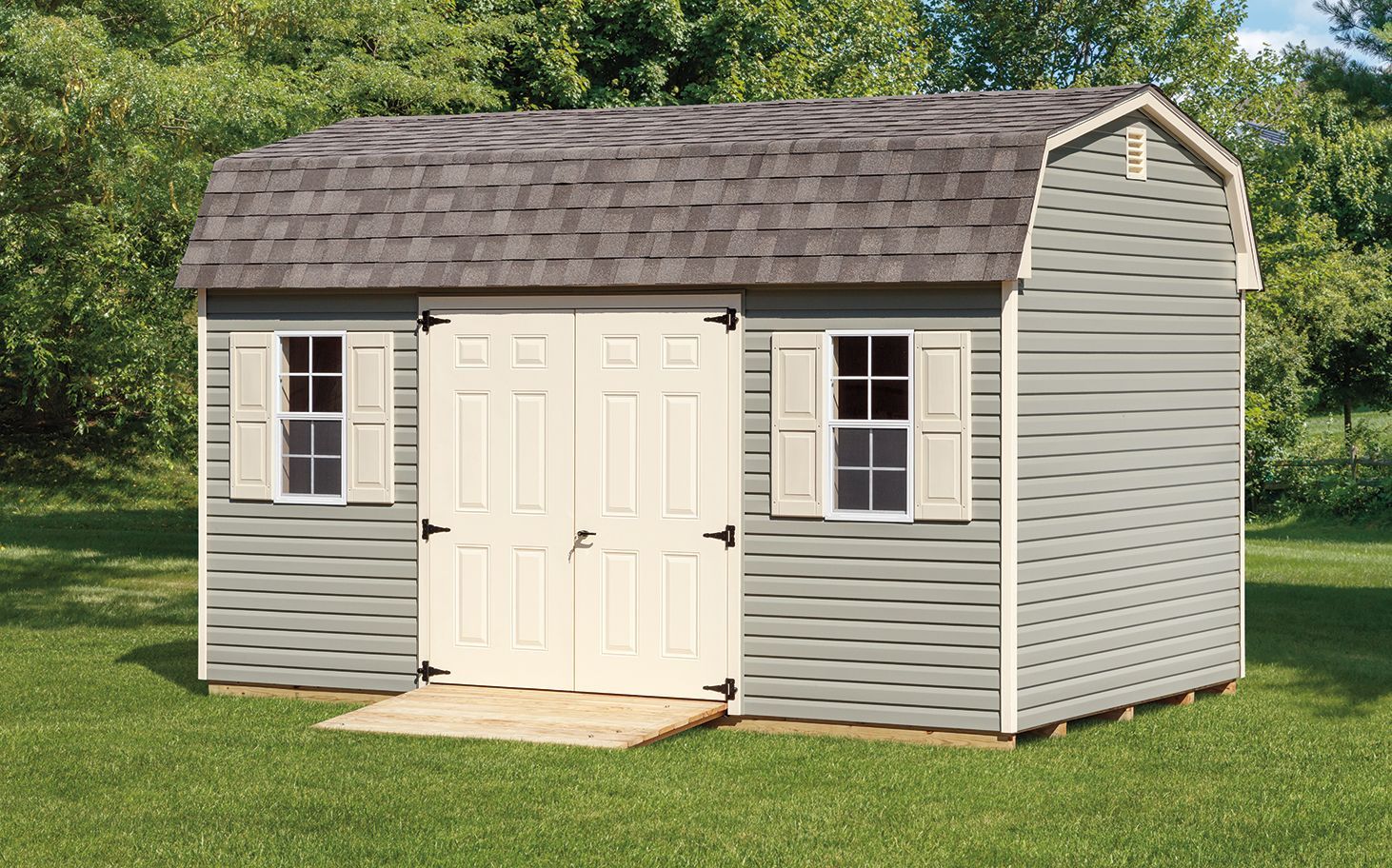 Gray shed with white door and window shutters, set on a green lawn.