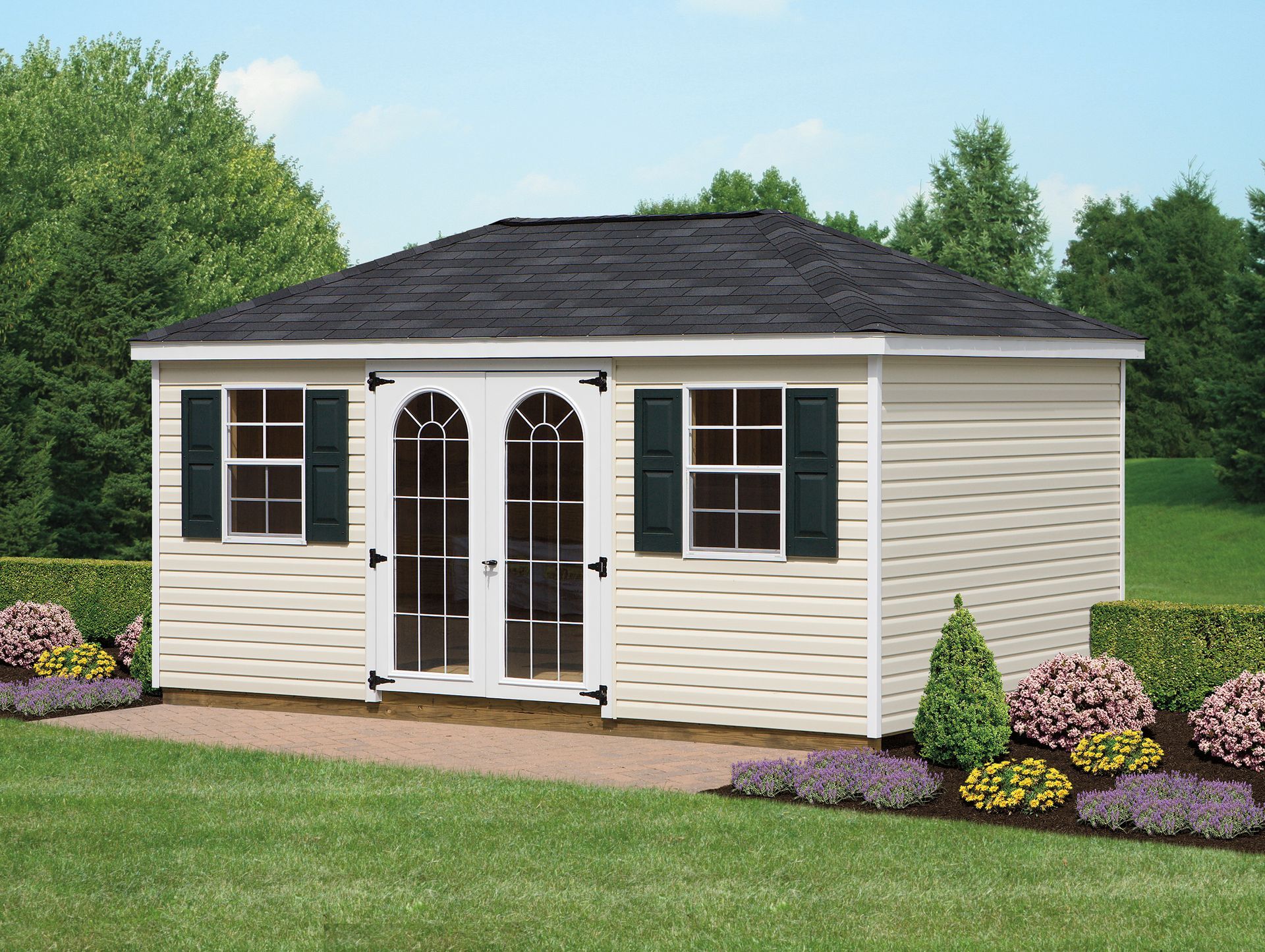 Tan shed with black roof, double arched doors, green shutters, and landscaping in a yard.
