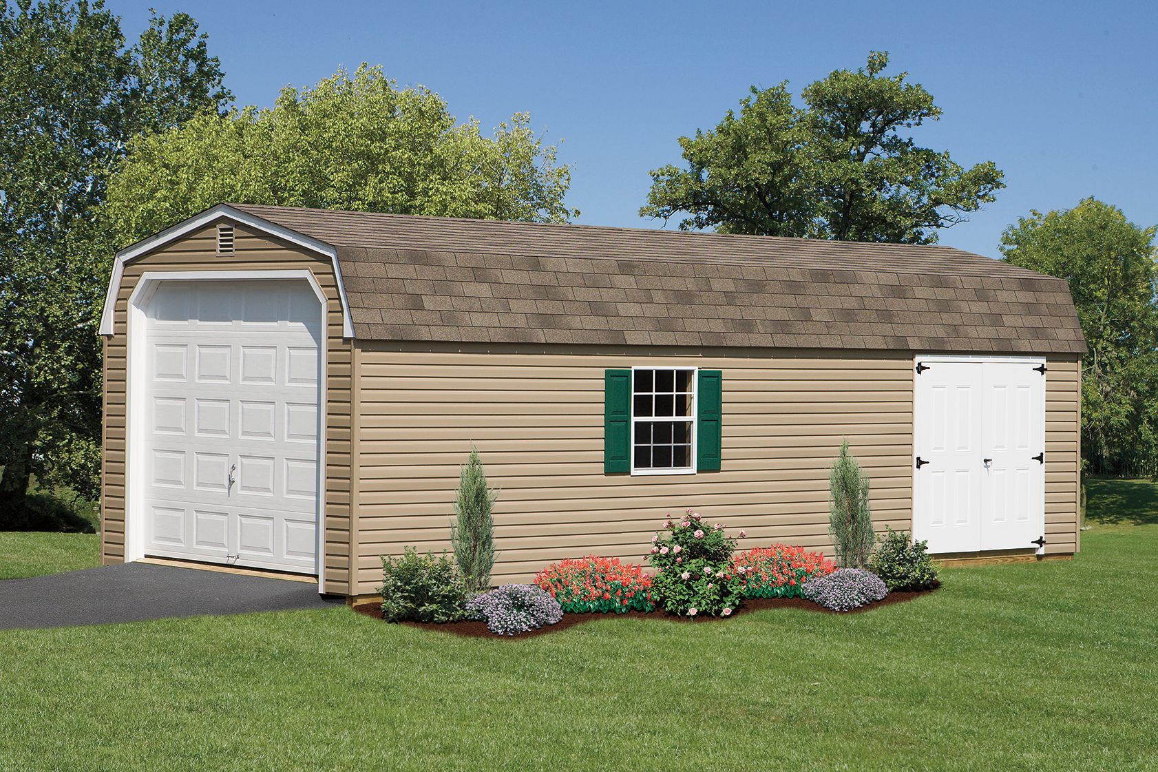 Tan shed with a garage door, small door, green shutters, and landscaping, on a grassy lawn.