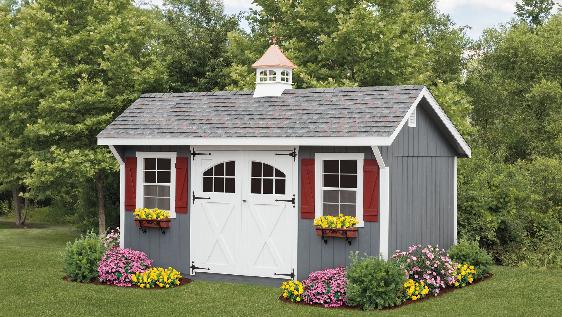 Gray shed with white doors, red shutters, and flower boxes in a grassy yard.