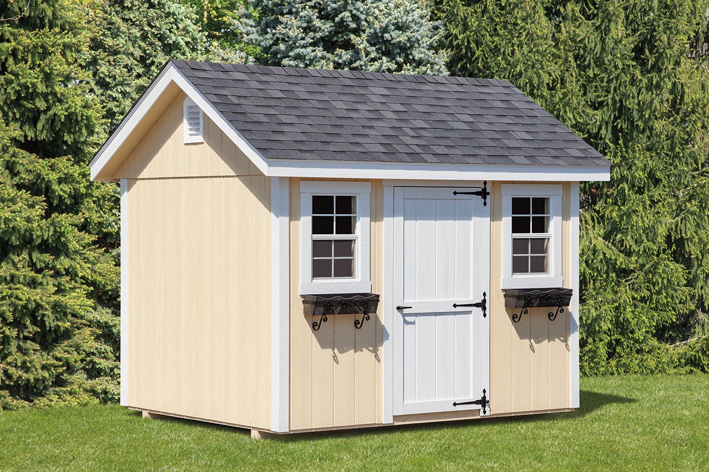 Tan shed with white trim, black roof and hardware, two windows with flower boxes, green grass, and trees.
