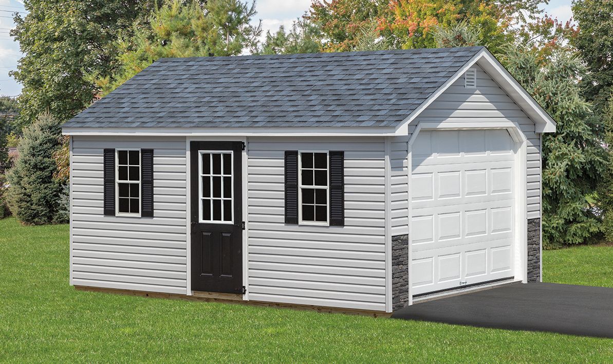 Small light gray shed with black door, windows, and shutters; white garage door, asphalt driveway.