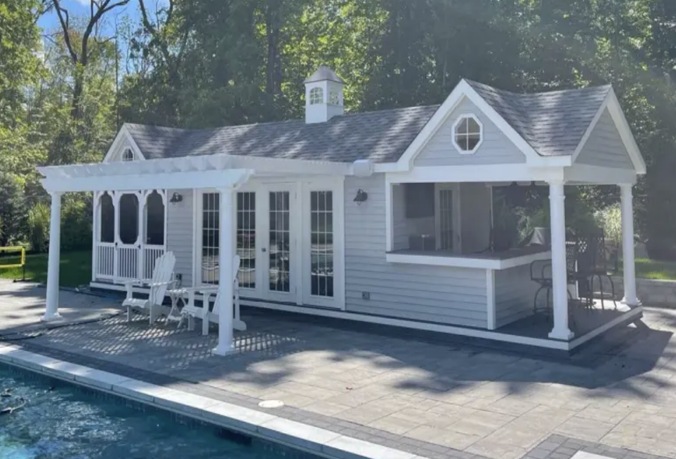 Poolside cabana with white pergola, light gray siding, and a bar.