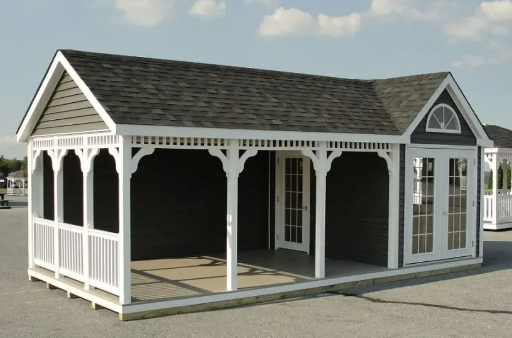 Small dark-colored building with white porch and detailed trim, gray roof, glass doors, and arched window.