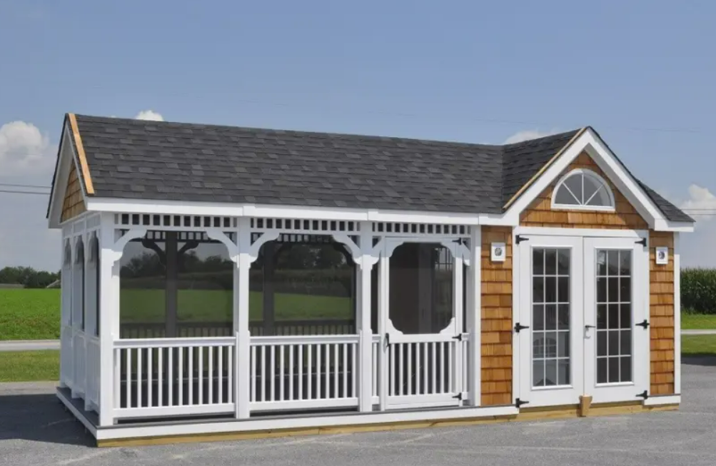 White and brown cottage-style shed with a porch and double doors, sitting on a wooden base.