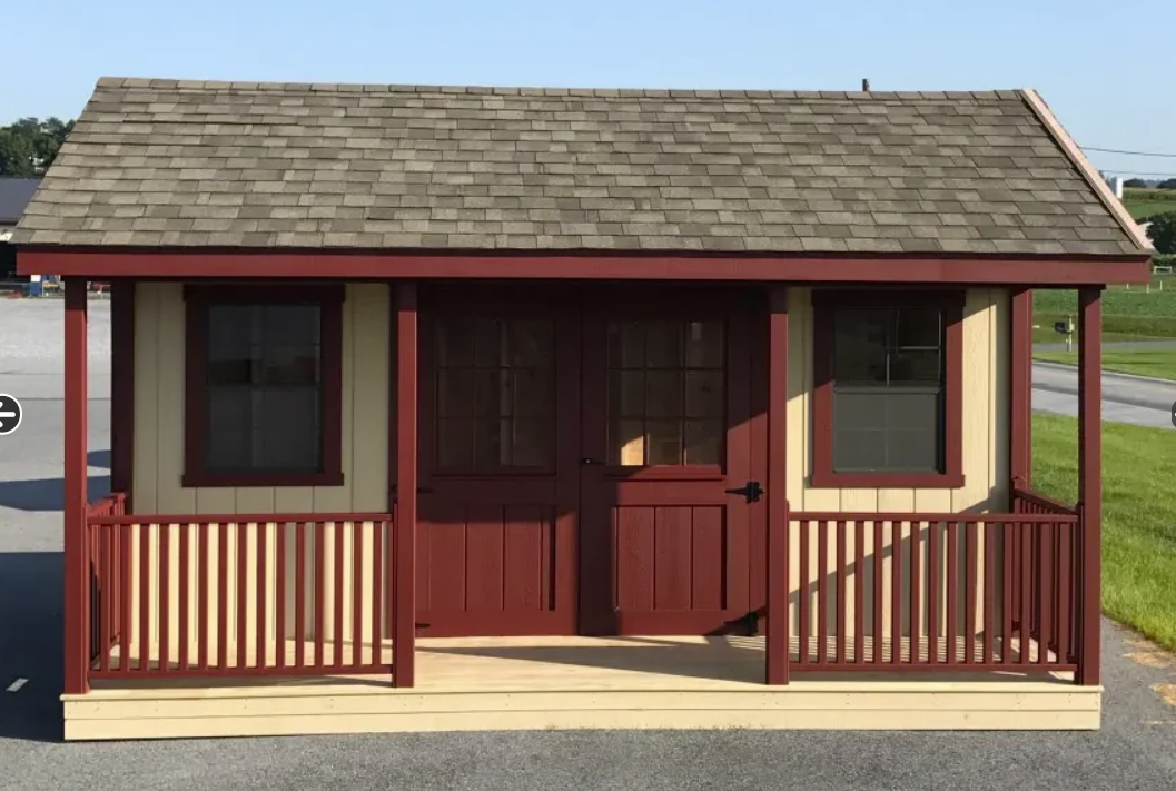 Small burgundy and tan shed with a porch and brown shingle roof.