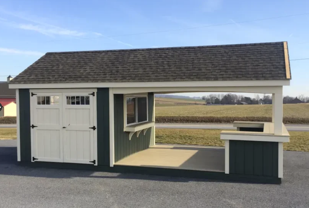 Green and white shed with a covered outdoor area and a serving counter in a rural setting.