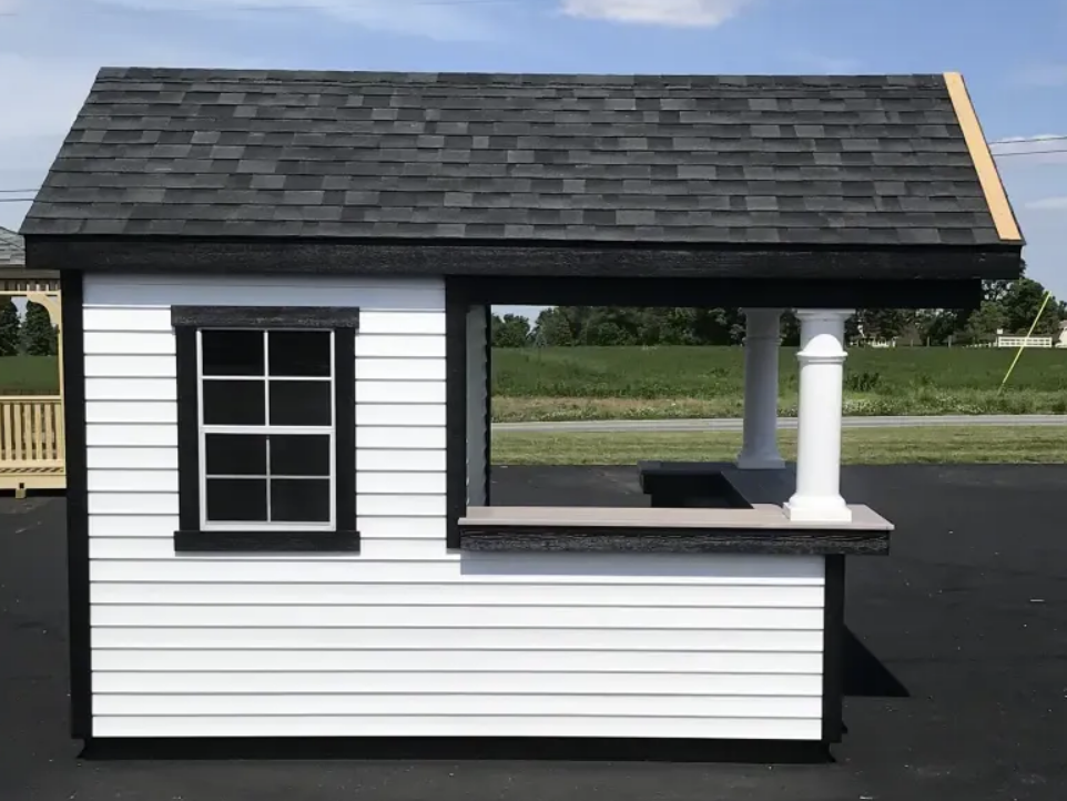 White and black playhouse with a black shingled roof, a window, and a counter.