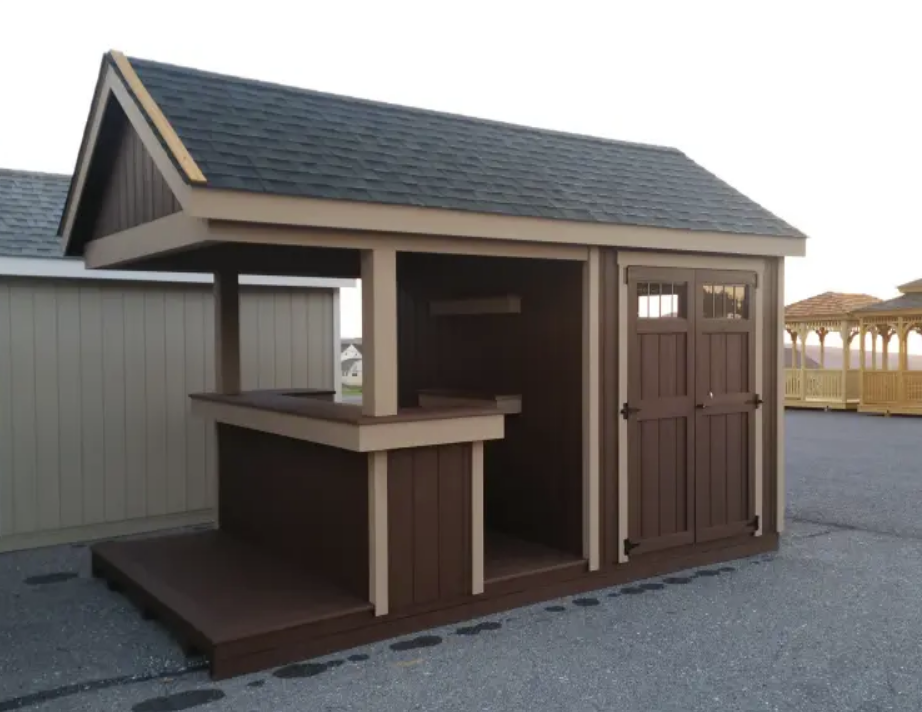 Brown outdoor shed with a bar area and a door, beige trim, dark roof.