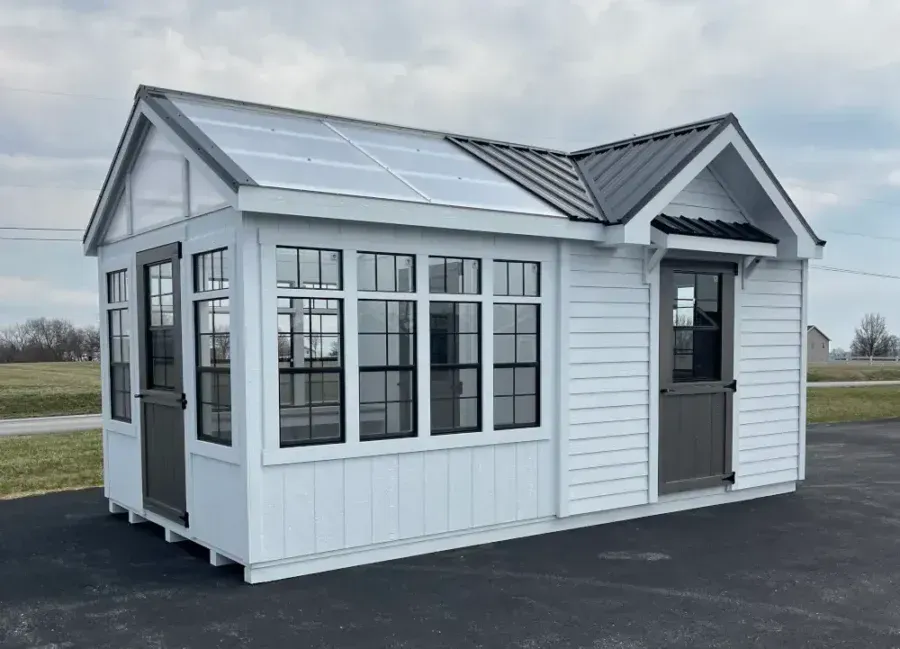 A white greenhouse and shed combination with glass roof panels, black window frames, and two dark gray doors.
