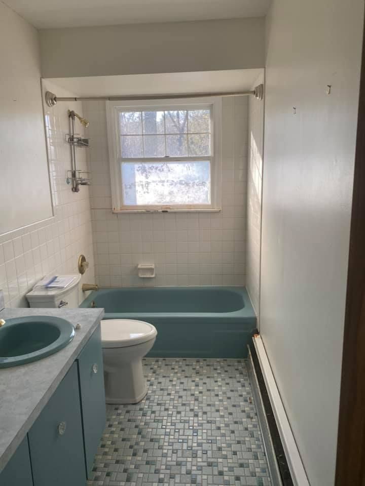 Small bathroom with teal sink, toilet, and bathtub, white tile walls, and a window above the tub. Small bathroom with teal sink, toilet, and bathtub, white tile walls, and a window above the tub.