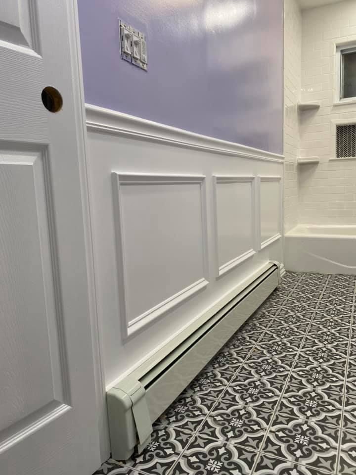 Hallway with white wainscoting, pale lavender wall, patterned carpet, and baseboard heater near a doorway Hallway with white wainscoting, pale lavender wall, patterned carpet, and baseboard heater near a doorway
