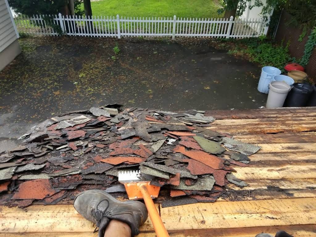 Roof shingles piled on a roof during repair, with a driveway and fence in the background Roof shingles piled on a roof during repair, with a driveway and fence in the background