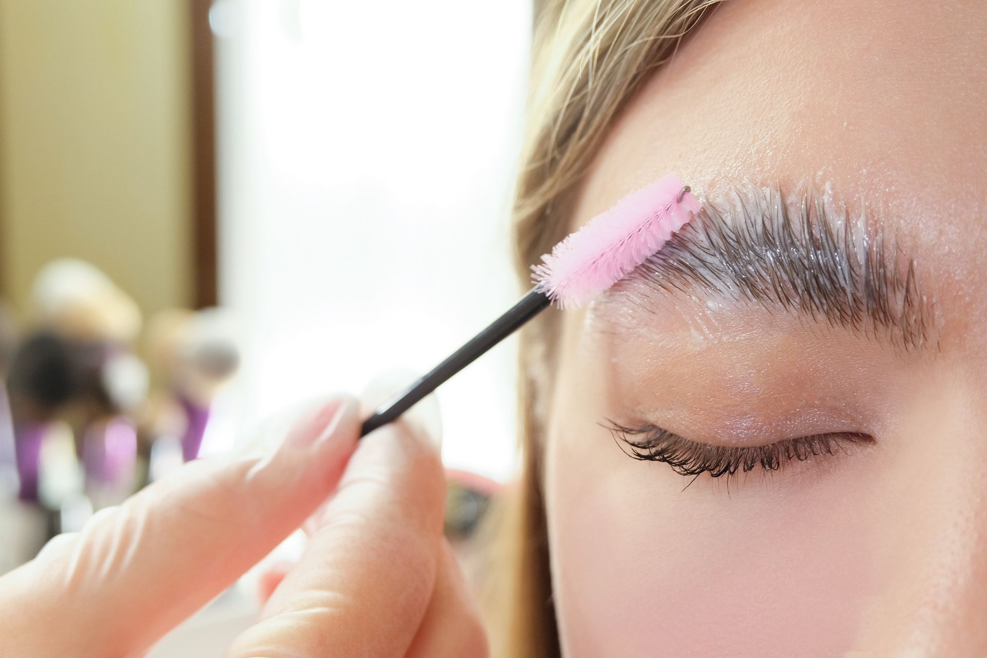 A woman is getting her eyebrows painted with a pink brush.