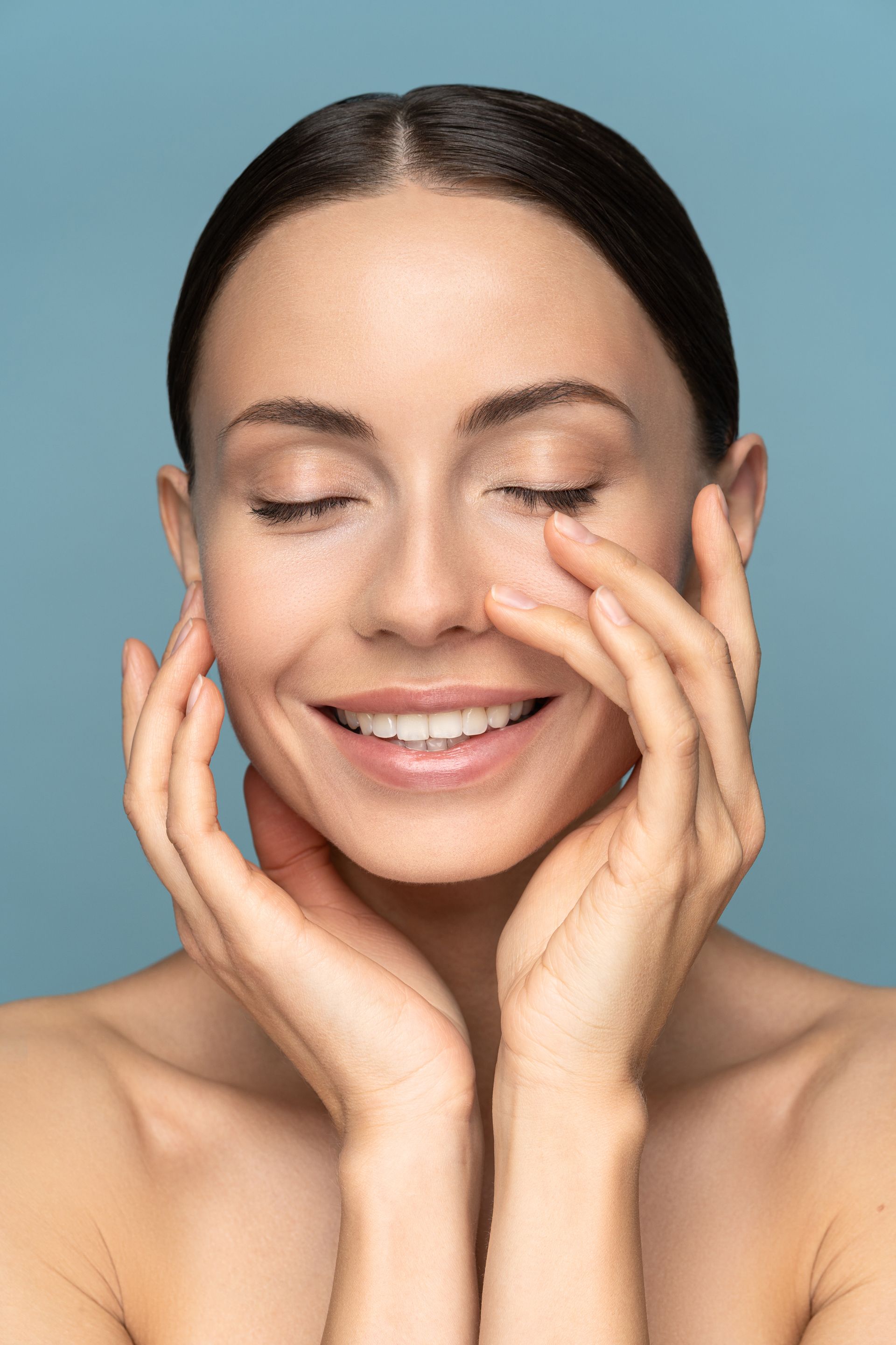 A woman is smiling and touching her face with her hands.