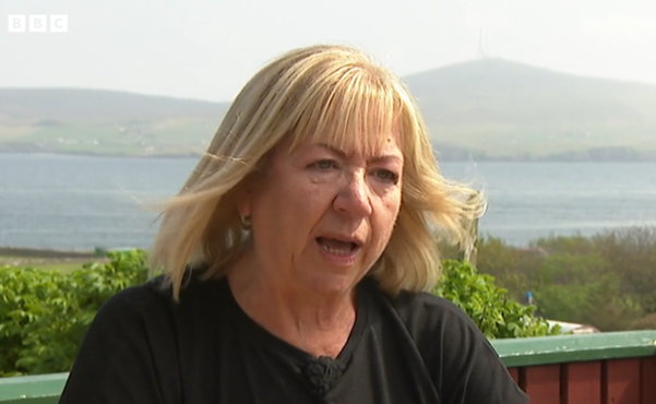 A woman in a black shirt is sitting on a balcony overlooking a body of water.