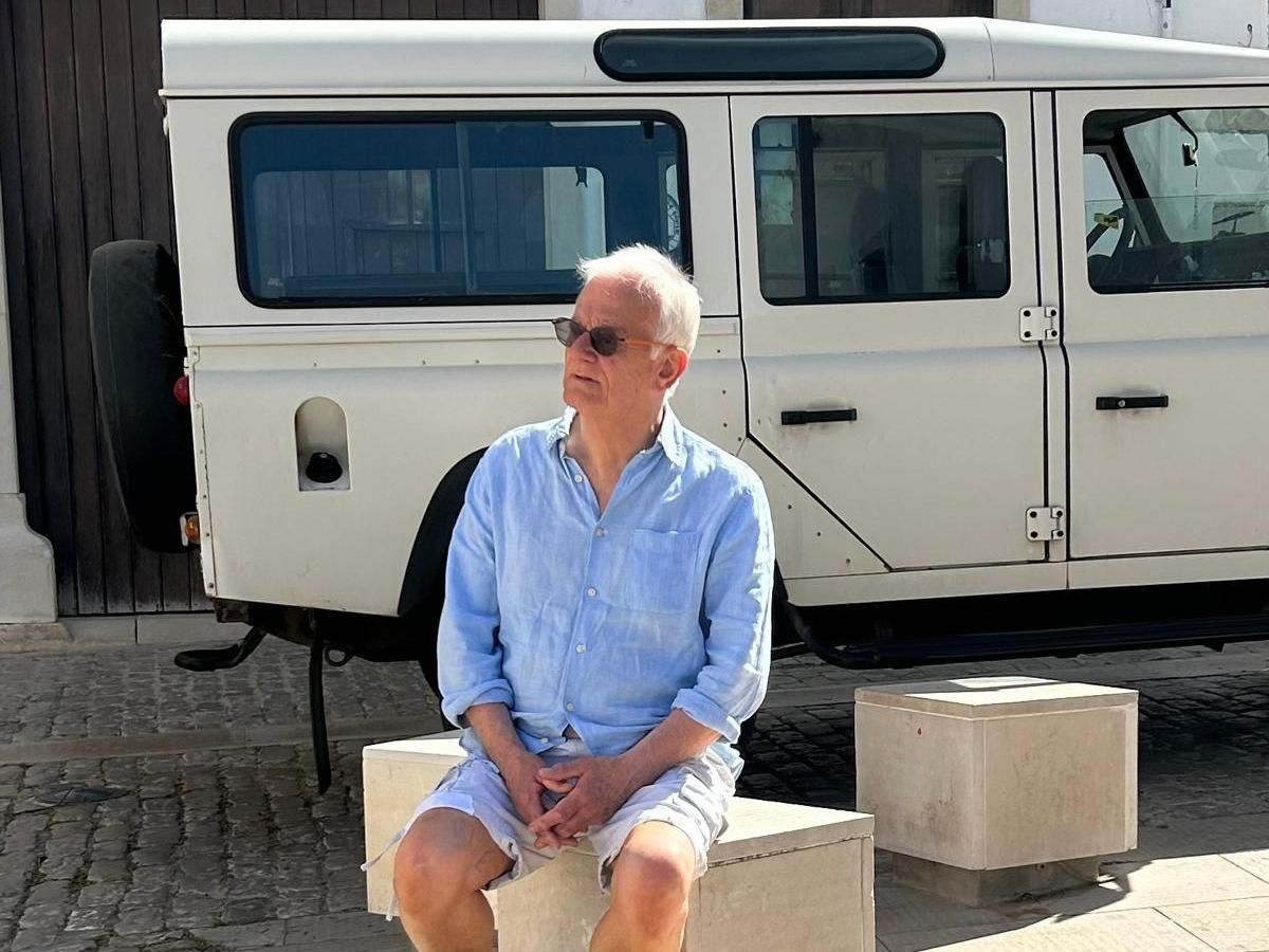 A man is sitting on a bench in front of a white van.