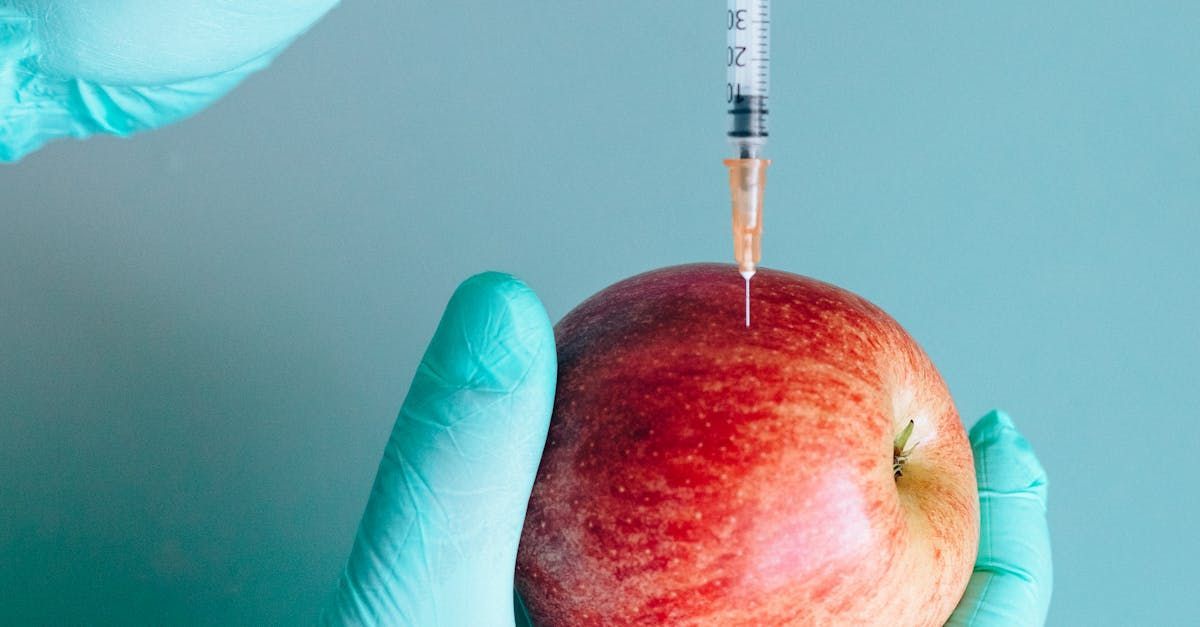 A person is holding an apple with a syringe in it.