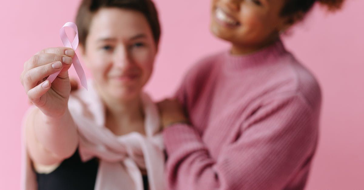 Two women are standing next to each other holding a pink ribbon.