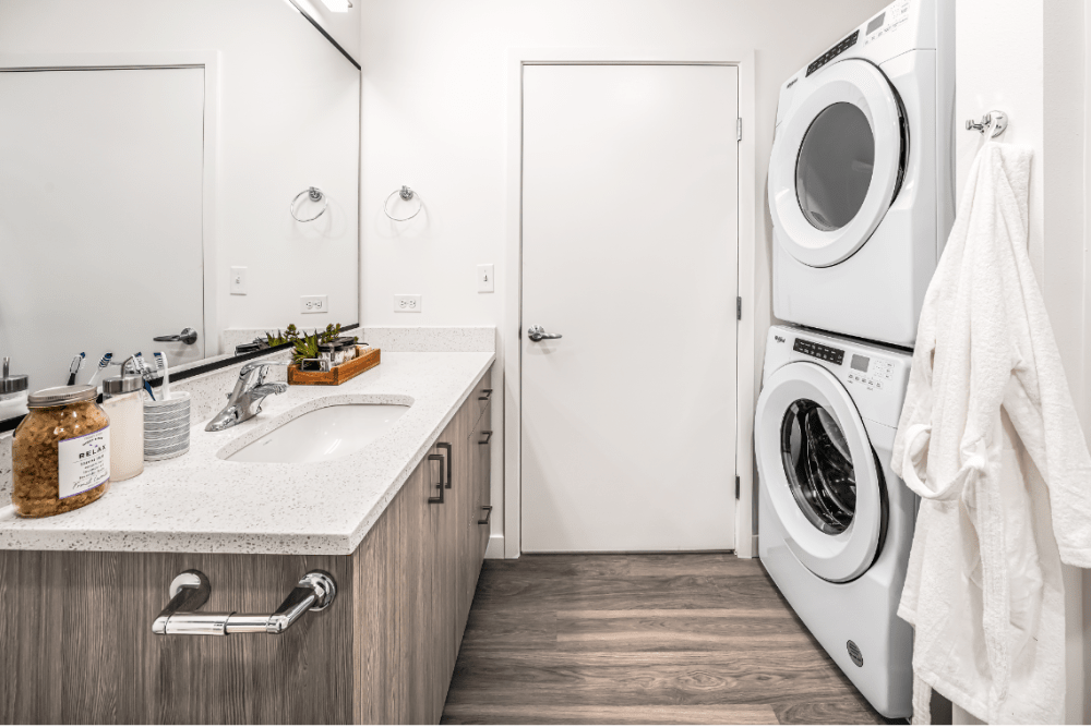 Indoor apartment laundry room with stacked washer/dryer, sink, and storage cabinets.