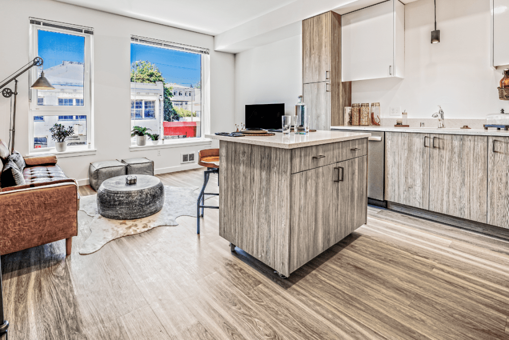 Open-concept kitchen and living area in a modern apartment with a central island and large windows.
