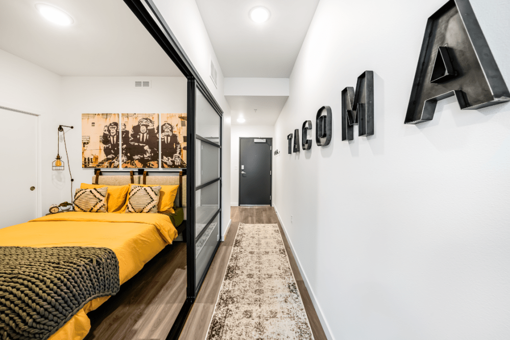 Bedroom with a glass partition, yellow bedding, and a hallway with bold metal letters on the wall.