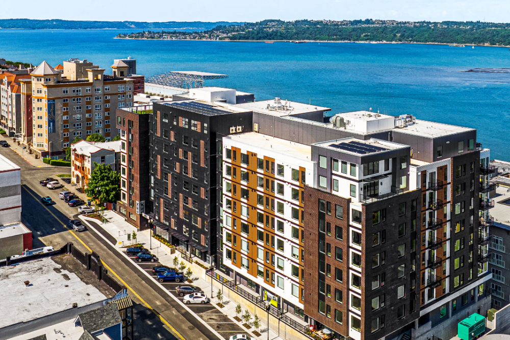 Aerial view of a modern multi-building apartment complex along a waterfront street.