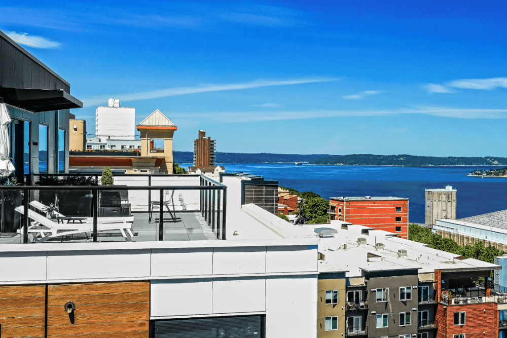 Rooftop terrace with lounge chairs and glass railing overlooking city and water.